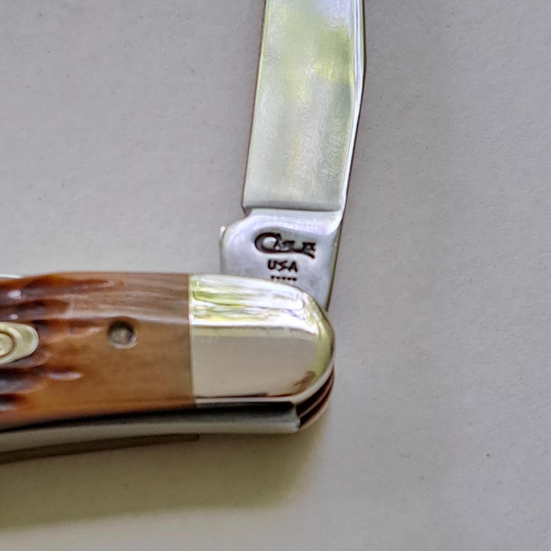 May include: Close-up of a partially open pocket knife. The blade is silver, and the handle is brown with a silver end. The knife has the text "Case USA" on the blade.