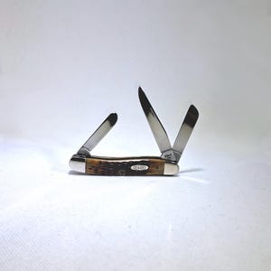 May include: A Case pocket knife with three stainless steel blades, two of which are open. The handle is brown with a textured pattern and a silver bolster. The word "CASE" is printed on the handle.