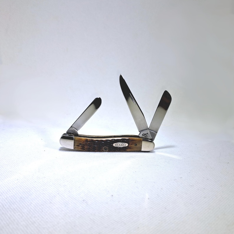May include: A Case pocket knife with three stainless steel blades, two of which are open. The handle is brown with a textured pattern and a silver bolster. The word "CASE" is printed on the handle.