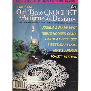 May include: A vintage crochet magazine cover from Fall 1984 featuring a white and purple crochet doily, a glass oil lamp, and a potted violet plant. The magazine title is "Old Time Crochet Patterns & Designs" with the text "Exciting Designs & Patterns from the Past to Make Today's Crocheting Interesting!"  The magazine lists crochet patterns for a flame vest, hooded scarf, sailboat desk set, sweetheart doll, afghan, and mittens.