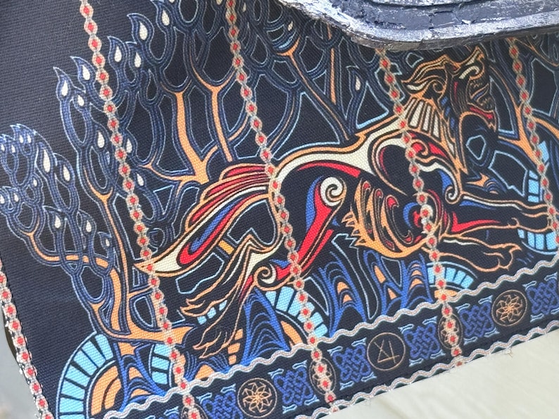 May include: Close-up of a fabric with a detailed, colorful design. The pattern features a stylized dragon or mythical creature in shades of red, blue, orange, and gold against a dark blue background. The design includes intricate lines and shapes.