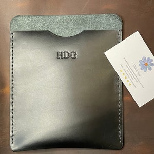 May include: Black leather wallet with a stitched edge and the initials "HDG" embossed on the front. A small white card with a blue flower and the text "Thank You" is next to the wallet.