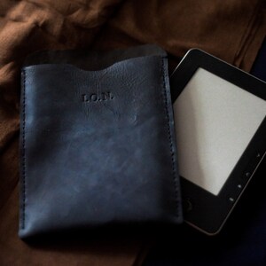 May include: A dark blue leather case with the initials "L.O.N." embossed on the front. A black e-reader is lying next to the case.