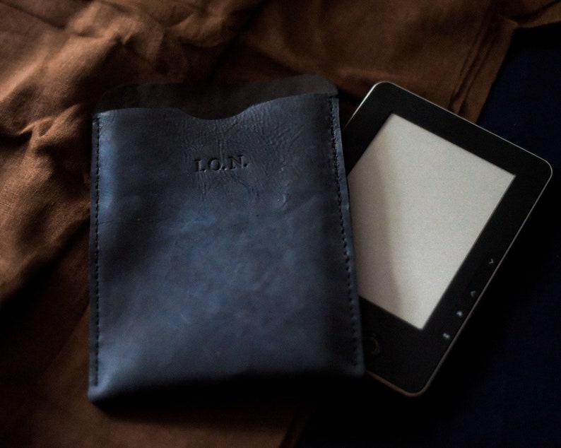 May include: A dark blue leather case with the initials "L.O.N." embossed on the front. A black e-reader is lying next to the case.