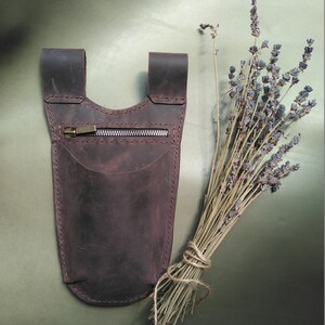 May include: A brown leather pouch with a zipper closure. The pouch has a strap that can be worn around the waist or shoulder.