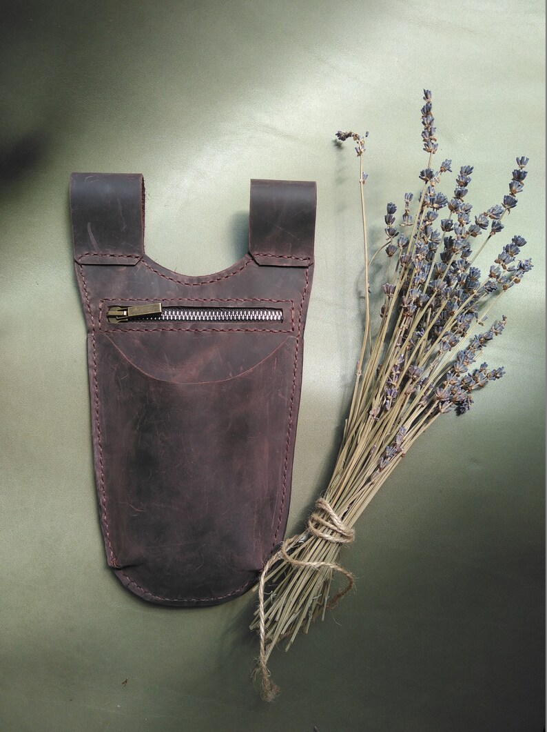May include: A brown leather pouch with a zipper closure. The pouch has a strap that can be worn around the waist or shoulder.