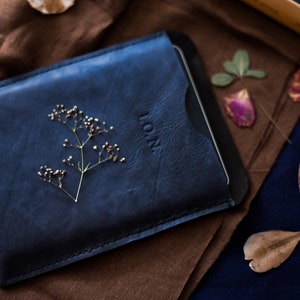 May include: A blue leather case with a small sprig of dried flowers and the word "L.O.N." embossed on the front.