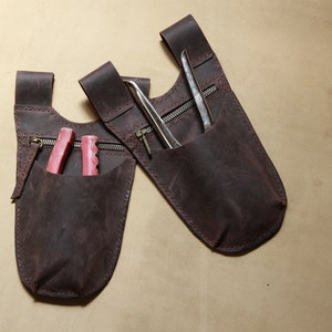 May include: Two brown leather tool pouches with zippered pockets. One pouch has a pair of pink pliers inside, and the other has a pair of metal tweezers.