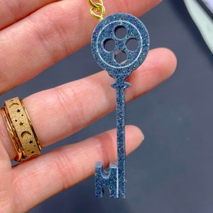 Puede incluir: Un llavero de llave plateado con un dise&ntilde;o de ojo de cerradura redondo de cuatro agujeros. El ojo de cerradura est&aacute; decorado con purpurina iridiscente.