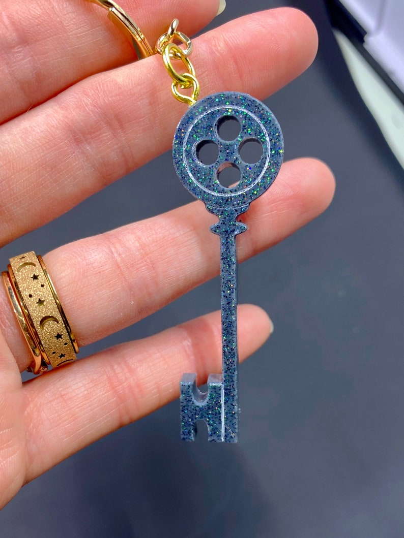 Puede incluir: Un llavero de llave plateado con un dise&ntilde;o de ojo de cerradura redondo de cuatro agujeros. El ojo de cerradura est&aacute; decorado con purpurina iridiscente.