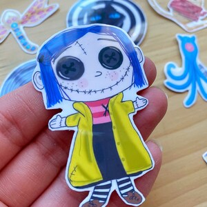 Puede incluir: Una pegatina con un personaje de dibujos animados con cabello azul, una chaqueta amarilla y medias a rayas blancas y negras. El personaje tiene ojos negros grandes con pupilas blancas y una boca cosida.