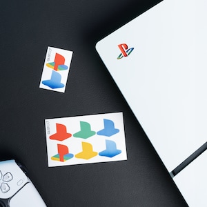 May include: Two sheets of stickers with a PlayStation logo and various colored controller symbols. The stickers are on a black surface.