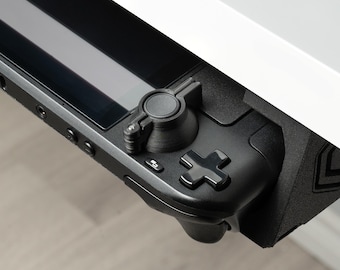 Op de afbeelding: Een zwarte handheld-gameconsole met een ronde knop aan de bovenkant en een kruisvormige knop aan de rechterkant.