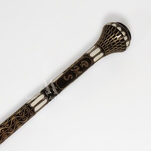 May include: A black walking stick with a white and gold decorative design. The top of the stick has a round, white knob with a gold design. The stick is engraved with the initials "R.M.S."