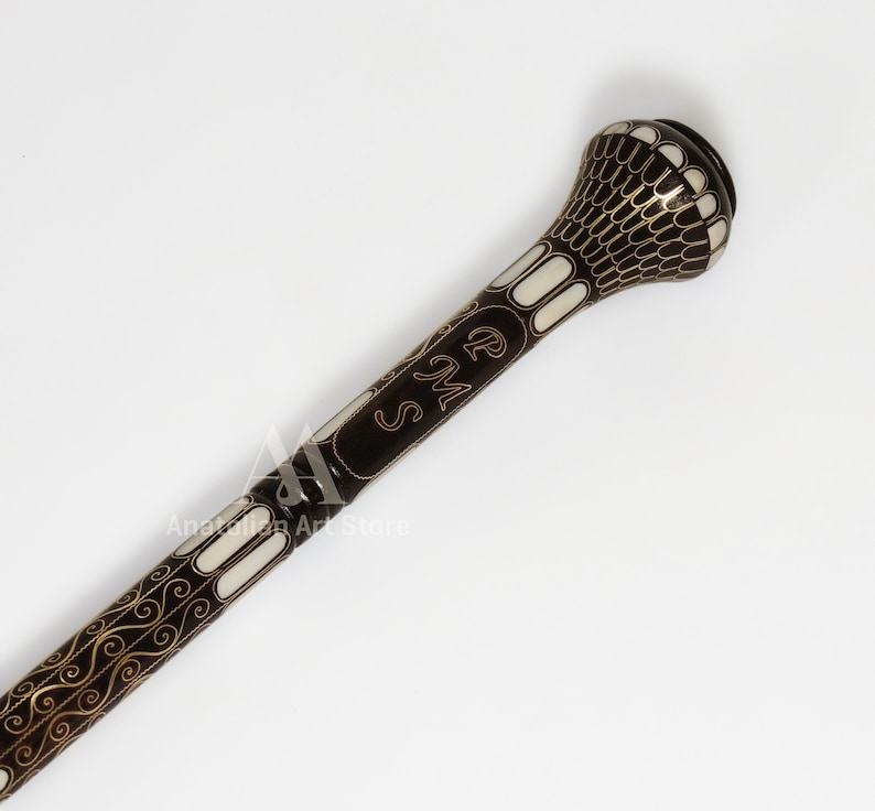 May include: A black walking stick with a white and gold decorative design. The top of the stick has a round, white knob with a gold design. The stick is engraved with the initials "R.M.S."