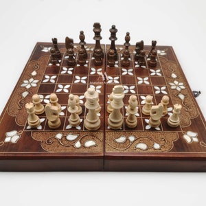 May include: A wooden chess set with a brown and white inlaid board. The board is decorated with floral patterns and mother-of-pearl accents. The chess pieces are made of wood and are painted in a light brown colour.