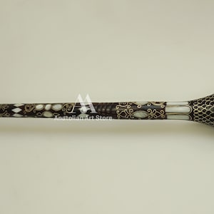 May include: A decorative walking stick with a dark brown wooden shaft and a white and gold inlaid design. The handle is a rounded, bulbous shape with a black and white pattern.