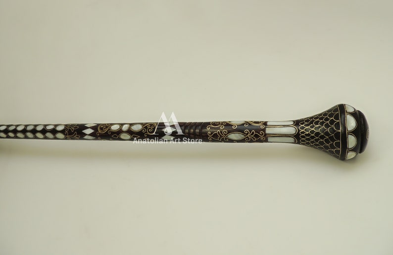 May include: A decorative walking stick with a dark brown wooden shaft and a white and gold inlaid design. The handle is a rounded, bulbous shape with a black and white pattern.