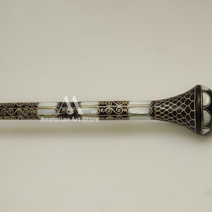 May include: A decorative walking stick with a black and white mother of pearl inlay and gold accents. The stick has a rounded knob at the top.