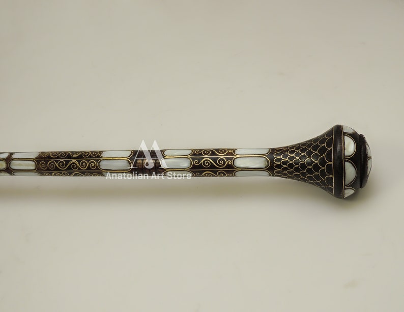 May include: A decorative walking stick with a black and white mother of pearl inlay and gold accents. The stick has a rounded knob at the top.