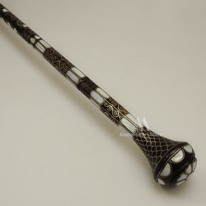 May include: A decorative walking stick with a dark brown wooden shaft and a pearlescent inlay design. The shaft is decorated with gold-colored swirls and the top of the stick has a pearlescent and gold-colored design.
