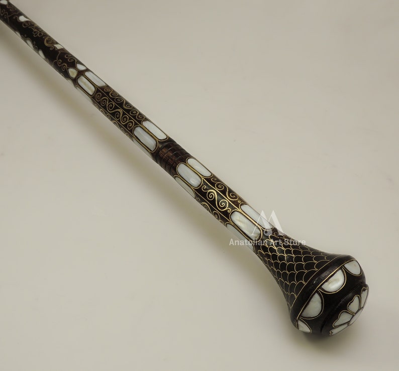 May include: A decorative walking stick with a dark brown wooden shaft and a pearlescent inlay design. The shaft is decorated with gold-colored swirls and the top of the stick has a pearlescent and gold-colored design.