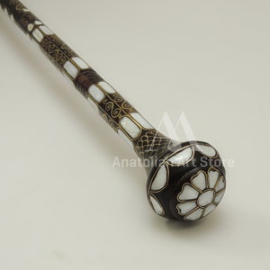 May include: A decorative walking stick with a dark brown wooden shaft and a white mother-of-pearl inlay design. The top of the stick is a round knob with a white flower design.