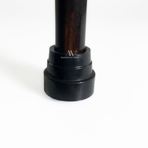 May include: Close-up of a dark brown wooden walking stick with a black rubber tip. The tip is layered and has a slightly rounded shape.