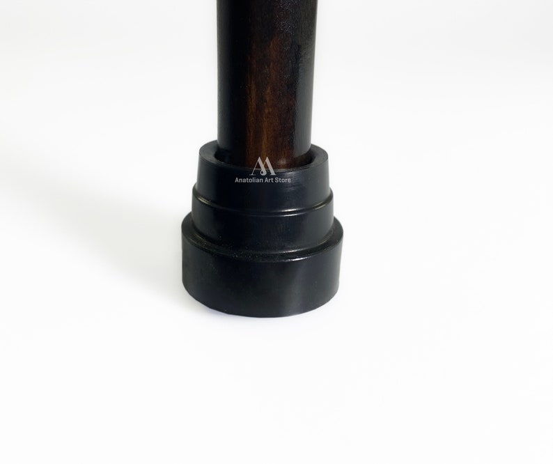 May include: Close-up of a dark brown wooden walking stick with a black rubber tip. The tip is layered and has a slightly rounded shape.