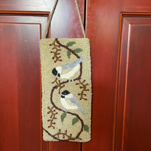 May include: A beige needlepoint wall hanging with a brown rope hanger. The design features two birds perched on branches with green leaves and red berries.