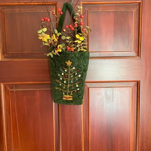 May include: A green felt stocking with a Christmas tree design and red berries hanging on a brown wooden door.