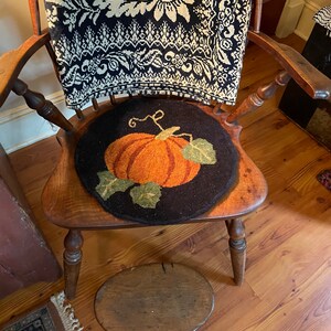 May include: A wooden chair with a black and white patterned throw blanket on the back and a pumpkin-shaped rug on the seat. A small wooden stool is in the foreground.
