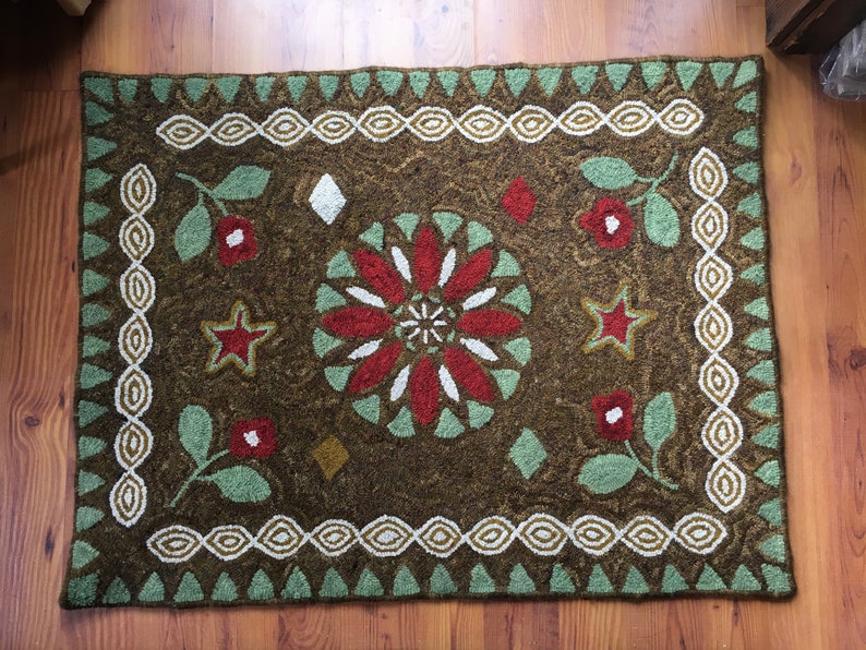 Op de afbeelding: Een bruin tapijt met een groen, wit en rood bloemenontwerp. Het tapijt heeft een witte en groene rand.