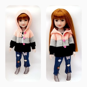 Puede incluir: Dos muñecas con un suéter de punto con capucha a rayas rosa, gris y negro con botones rosas. Las muñecas llevan pantalones vaqueros azules con flores y mariposas bordadas.