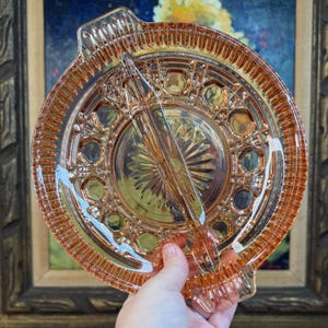 May include: A divided pink glass dish with a scalloped edge and a floral pattern. The dish is made of pressed glass and has a vintage look.