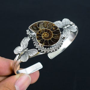 May include: Silver bracelet with a brown ammonite fossil and two silver butterfly accents.
