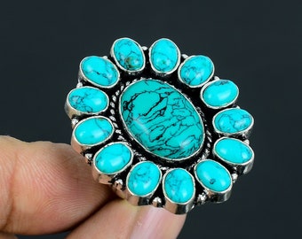 Puede incluir: Un anillo turquesa con una gran piedra ovalada turquesa rodeada de piedras turquesa más pequeñas. El anillo está hecho de plata y tiene un diseño floral.