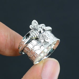 May include: A silver ring with a bee design and a honeycomb pattern. The ring is adjustable and can be worn on any finger.