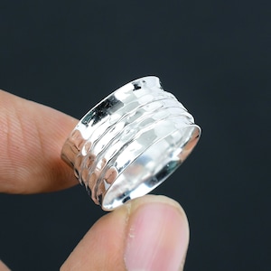 Può includere: Un anello girevole in argento con una texture martellata. L'anello è largo e ha una forma arrotondata.