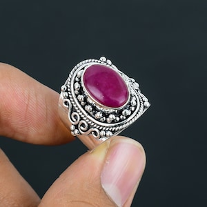 Könnte beinhalten: Ein silberner Ring mit einem ovalen rosafarbenen Edelstein, der in einer detaillierten silbernen Fassung sitzt. Der Ring hat ein breites Band mit aufwendigen Schnörkeln und Perlen.