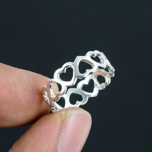 May include: A silver ring featuring a delicate design of interlocking hearts. The ring is crafted from smooth, polished metal and has a simple, elegant appearance.