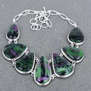May include: A silver necklace with a teardrop-shaped pendant made of green and purple gemstone. The necklace has a chain link design.