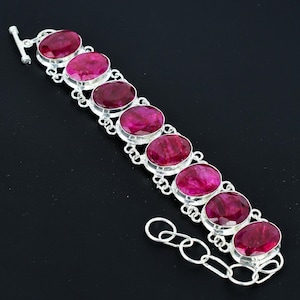 Peut inclure: Un bracelet en argent orné de pierres précieuses roses foncées de forme ovale. Les pierres sont serties dans des chatons individuels en argent et reliées par des maillons en argent. Le bracelet a une fermeture à bascule. Les pierres mesurent environ 2 cm de long.