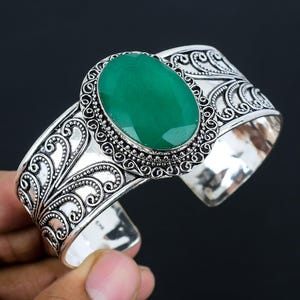 Puede incluir: Un brazalete de plata con un diseño adornado que presenta una gran piedra preciosa ovalada verde.