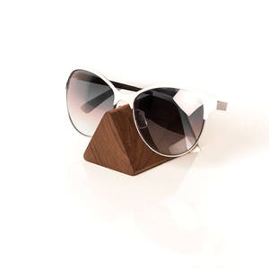 Könnte beinhalten: Weiße Sonnenbrille mit dunklen Gläsern, die auf einem dreieckigen Holzständer ruht.