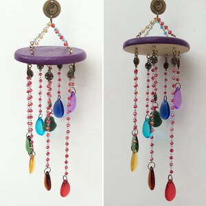 May include: A purple wooden circular base with a yin yang symbol hanging from the top.  The base has multiple strands of beads with colorful glass drops hanging from them.  The beads are red, green, blue, and purple.