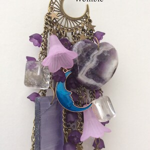 Pu&ograve; includere: Un ciondolo a forma di collana steampunk viola e blu con una mezzaluna, stelle e cristalli di ametista. Il testo "Steampunk Womble" &egrave; visibile sul ciondolo.