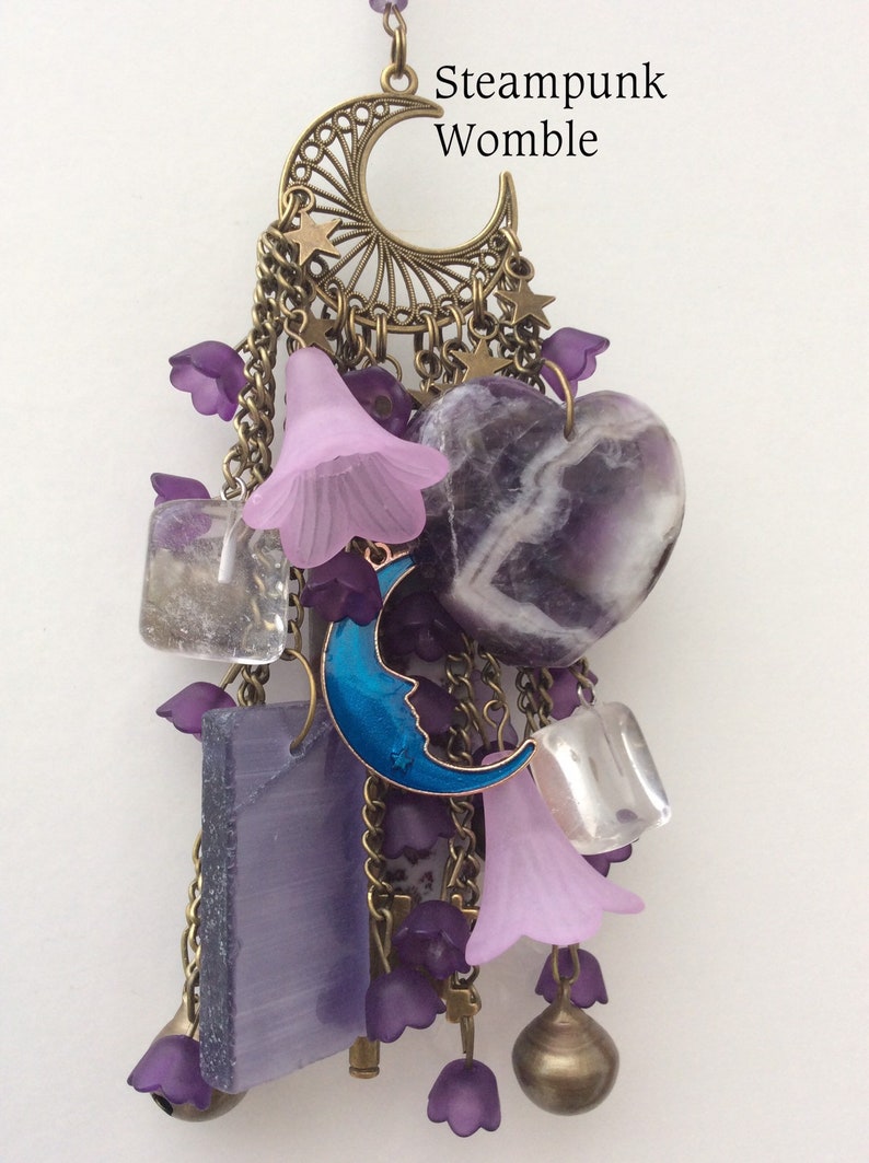 Pu&ograve; includere: Un ciondolo a forma di collana steampunk viola e blu con una mezzaluna, stelle e cristalli di ametista. Il testo "Steampunk Womble" &egrave; visibile sul ciondolo.