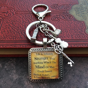 Può includere: Un portachiavi color argento con un ciondolo quadrato recante il testo Life Is Infinitely Stranger Than Anything Which The Mind Of Man Could Invent Sherlock Holmes, A Case Of Identity (1891) e ciondoli a forma di torre, pipa, violino e chiave.