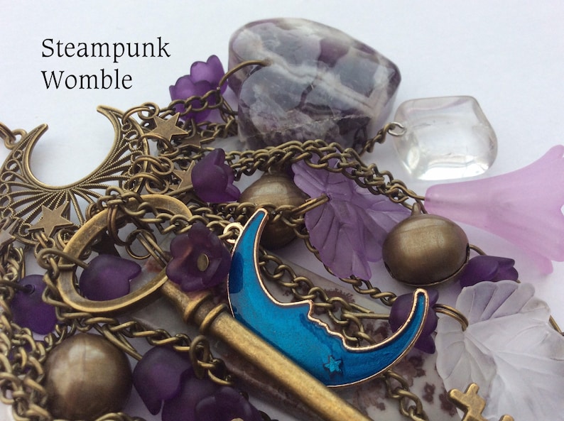 Pu&ograve; includere: Un braccialetto con ciondoli a tema steampunk con una chiave, ciondoli a forma di luna, fiori viola e una grande pietra di ametista.